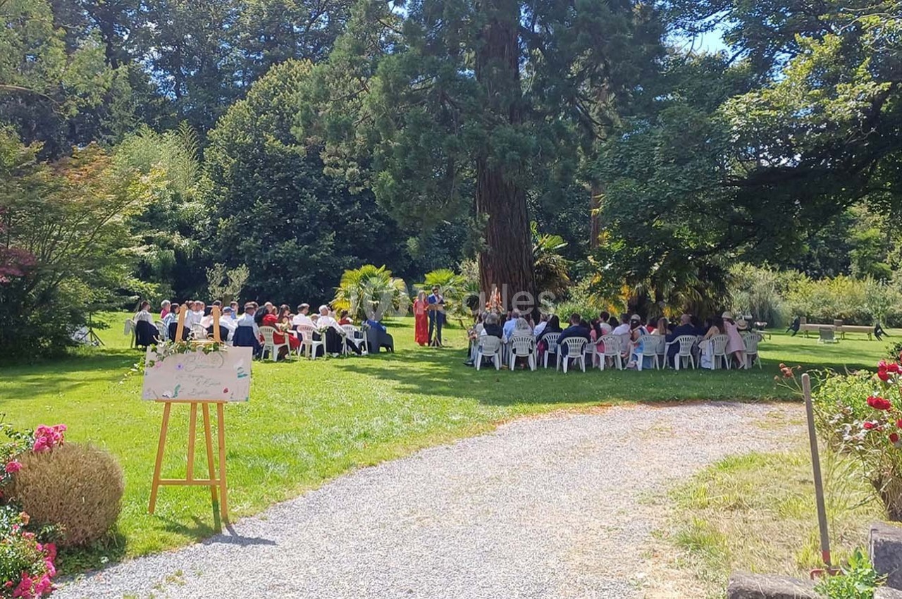 Groupe de personnes assises en plein air dans un jardin, entourées d'arbres et de fleurs, avec un chevalet au premier plan.