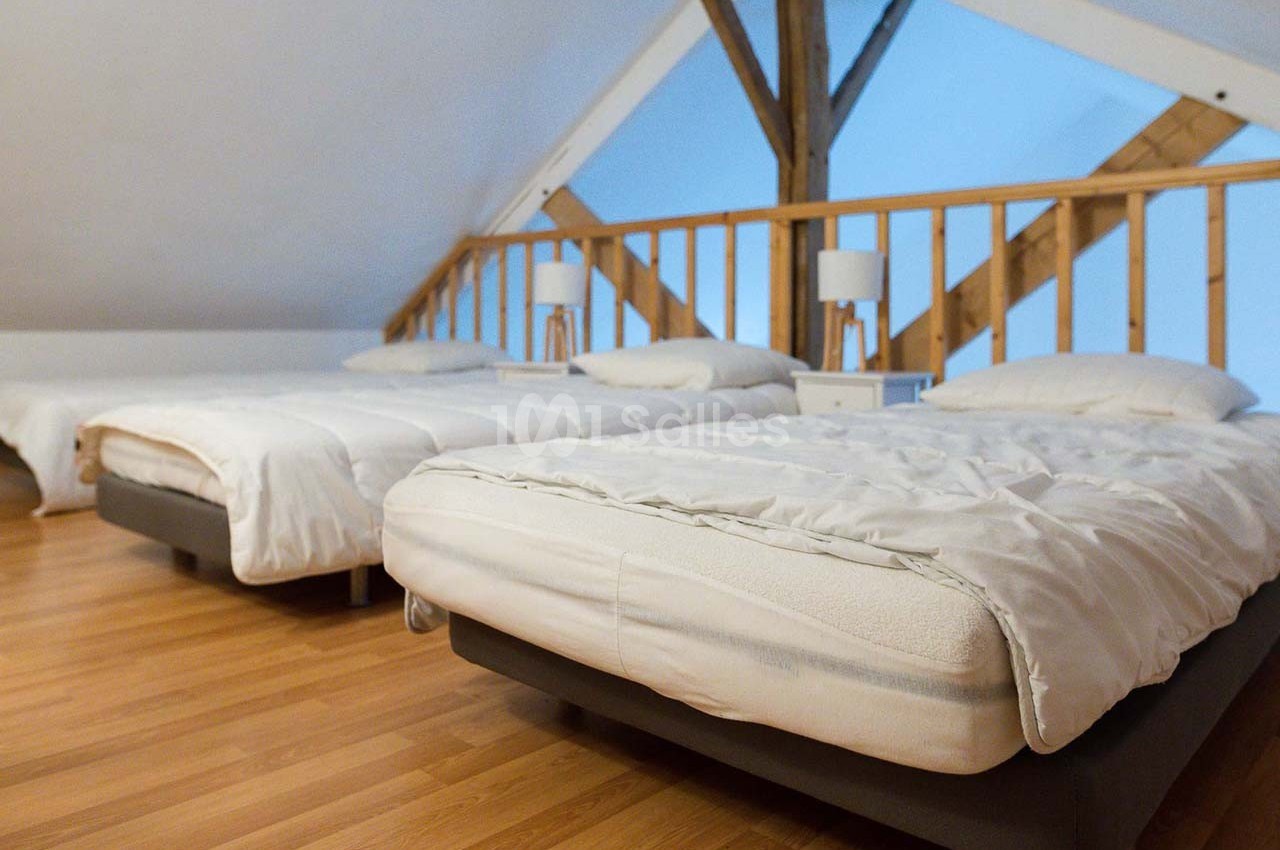 Trois lits simples alignés dans une chambre mansardée avec parquet et poutres apparentes.