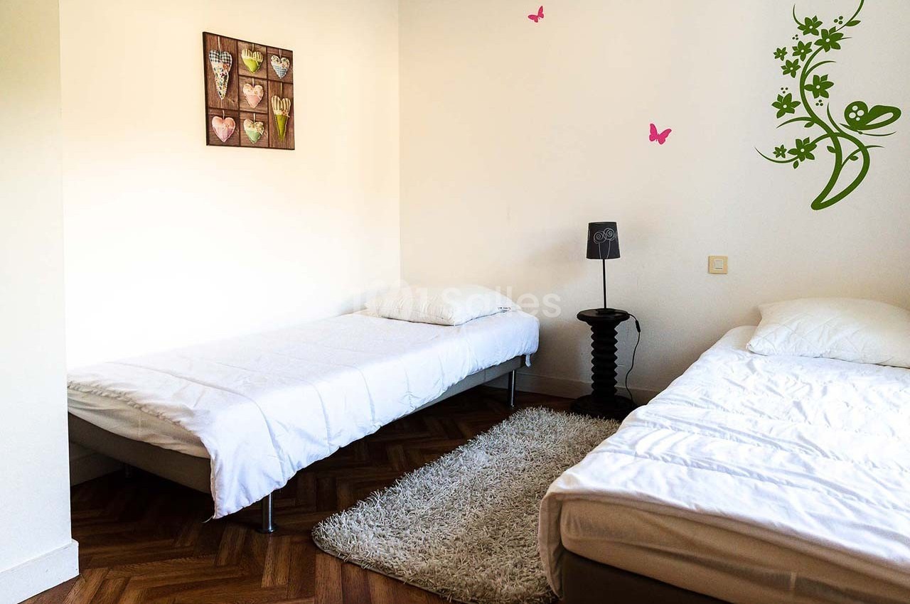 Deux lits simples dans une chambre lumineuse avec parquet, décorée de cadres et motifs muraux.