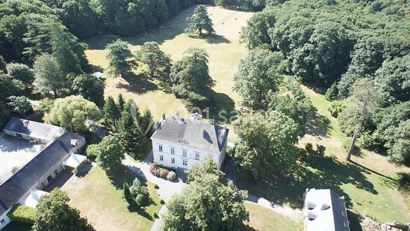 Vue aérienne d'un manoir entouré de jardins, de prairies et d'une forêt dense en arrière-plan.