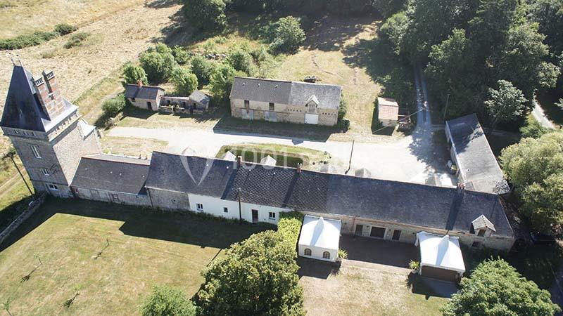 Vue aérienne d'un domaine rural avec bâtiments en pierre, une tour, des toits en ardoise et des espaces verts.