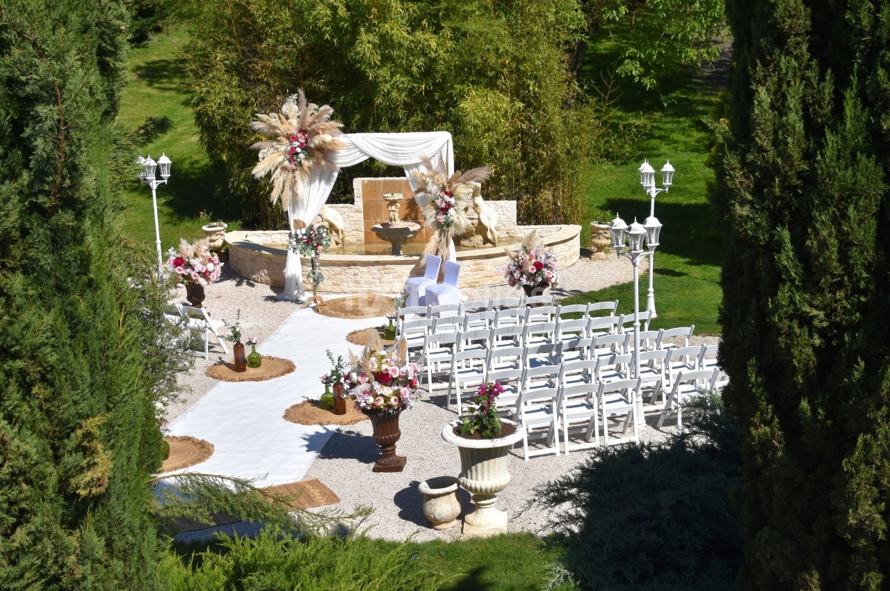 Cérémonie de mariage en plein air avec chaises blanches alignées, arche décorée de fleurs et végétation environnante.