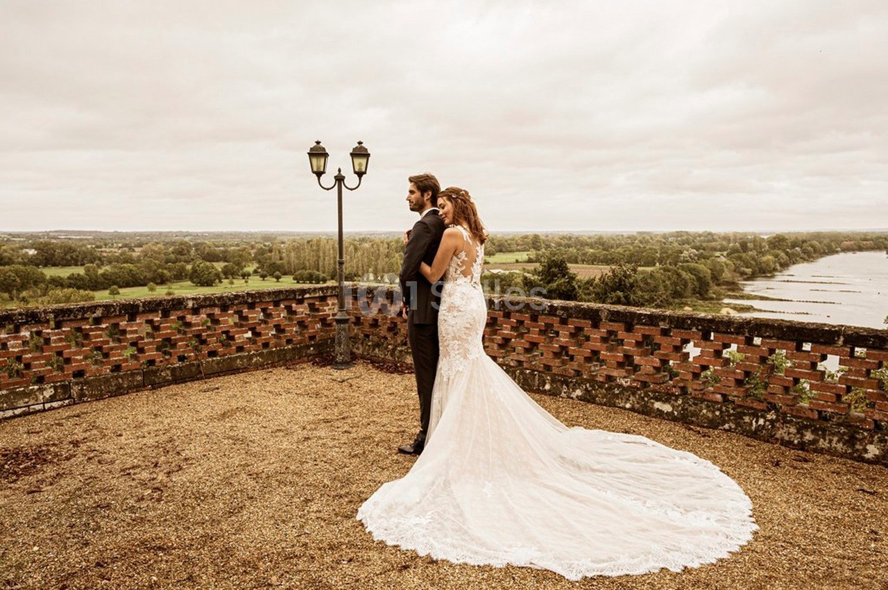 Un couple en tenue de mariage se tient sur une terrasse surplombant un paysage verdoyant et un cours d'eau.