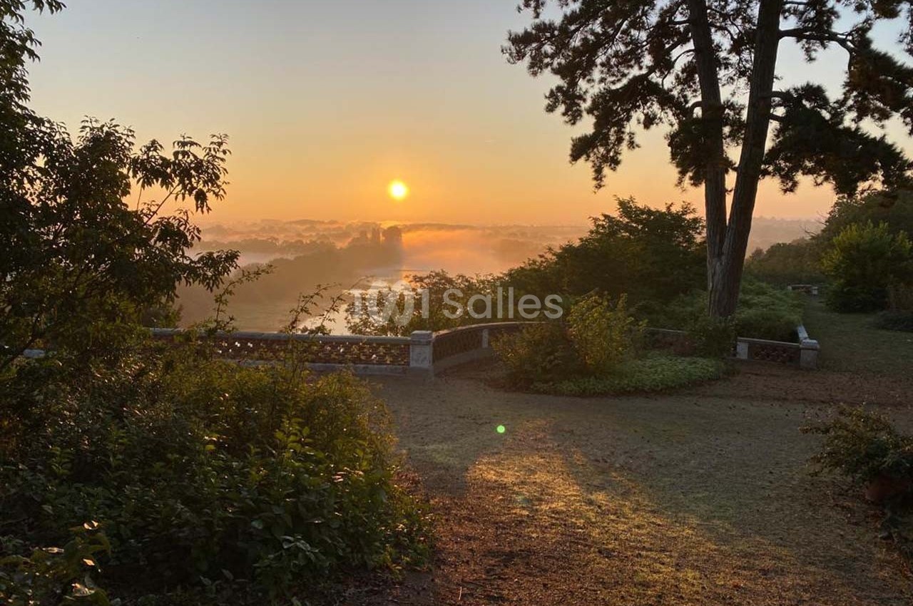 Lever de soleil illuminant un jardin avec des arbres, un muret en pierre et une vue sur un paysage brumeux.