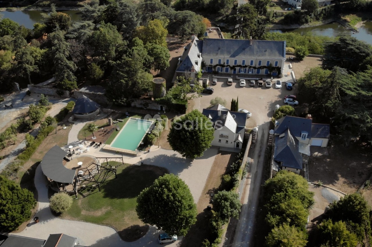 Vue aérienne d'un domaine avec bâtiments anciens, piscine, espaces verts et un parking, entouré de végétation.