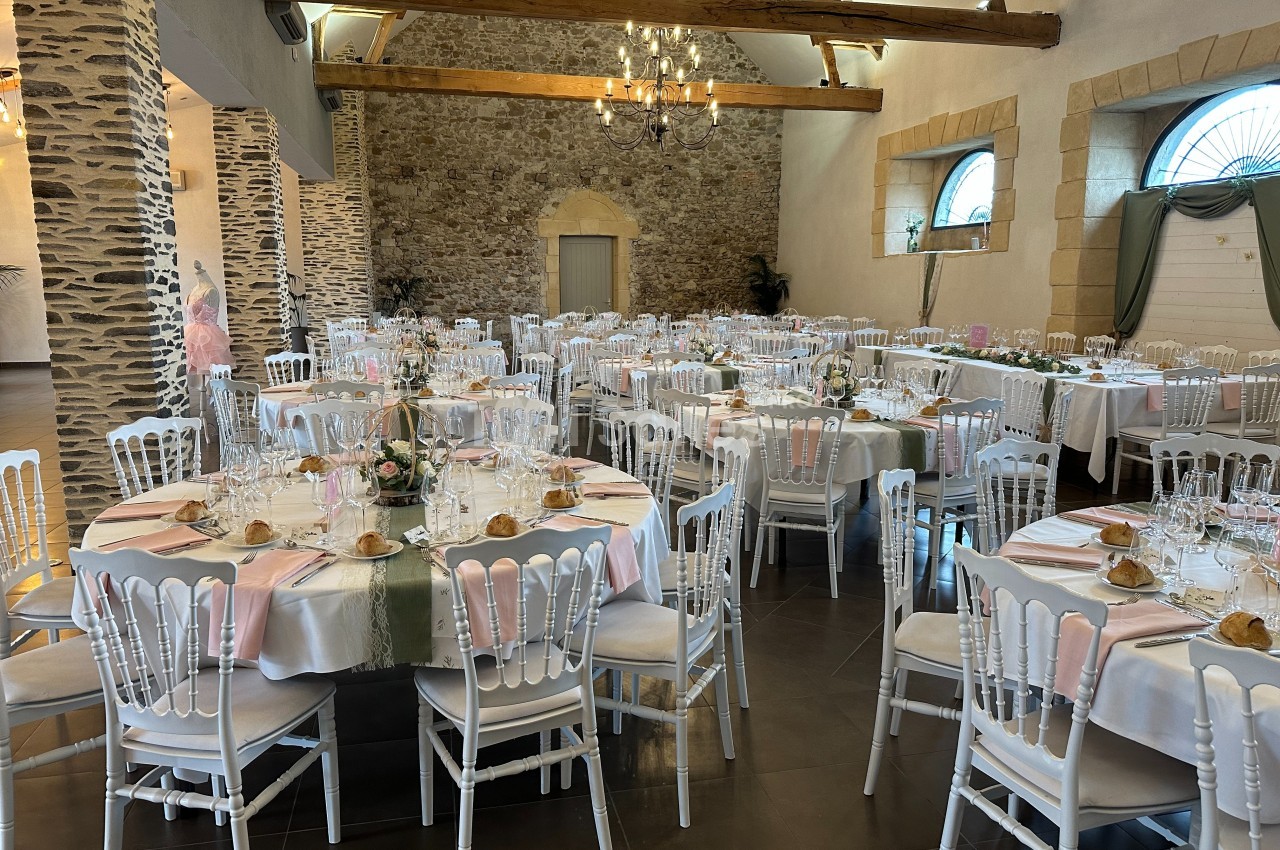 Salle de réception décorée avec des tables rondes dressées, nappes blanches et chaises blanches, ambiance élégante.