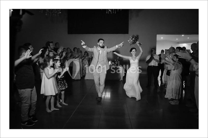 Un couple de mariés entre dans une salle de réception, acclamé par des invités applaudissant.