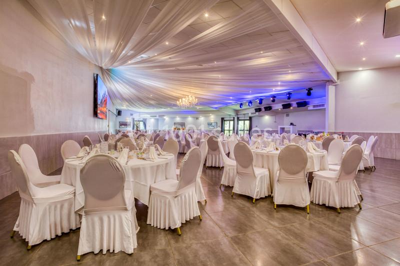 Salle de réception élégante avec tables rondes dressées, chaises blanches et plafond drapé illuminé.