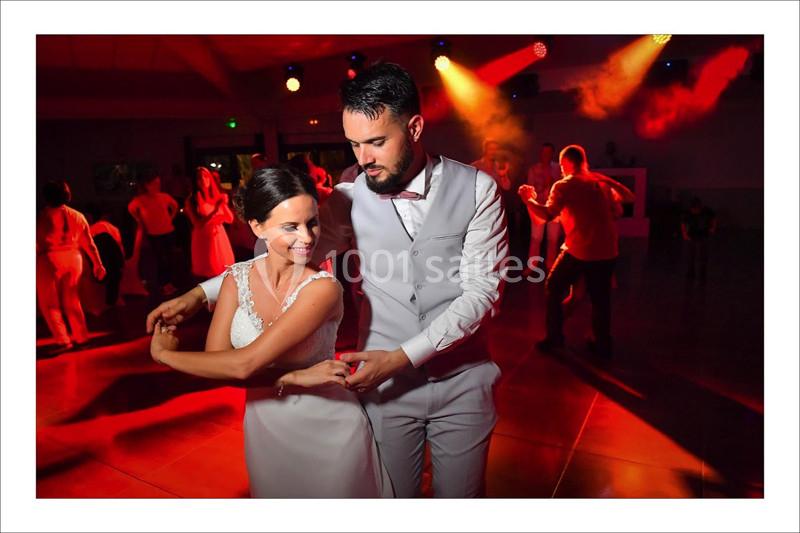 Un couple danse élégamment dans une salle éclairée par des lumières colorées, entouré d'autres invités.