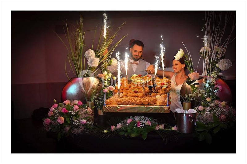 Un couple de mariés coupe une pièce montée entourée de fleurs et de fontaines lumineuses.