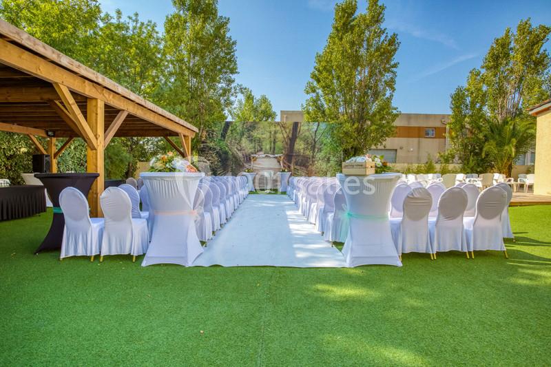 Allée centrale bordée de chaises blanches sur une pelouse, avec un décor naturel et une pergola en bois à gauche.