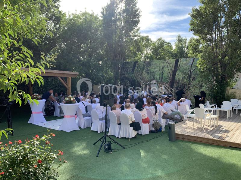 Cérémonie en plein air avec des invités assis sur des chaises blanches, entourés de verdure et d'arbres.