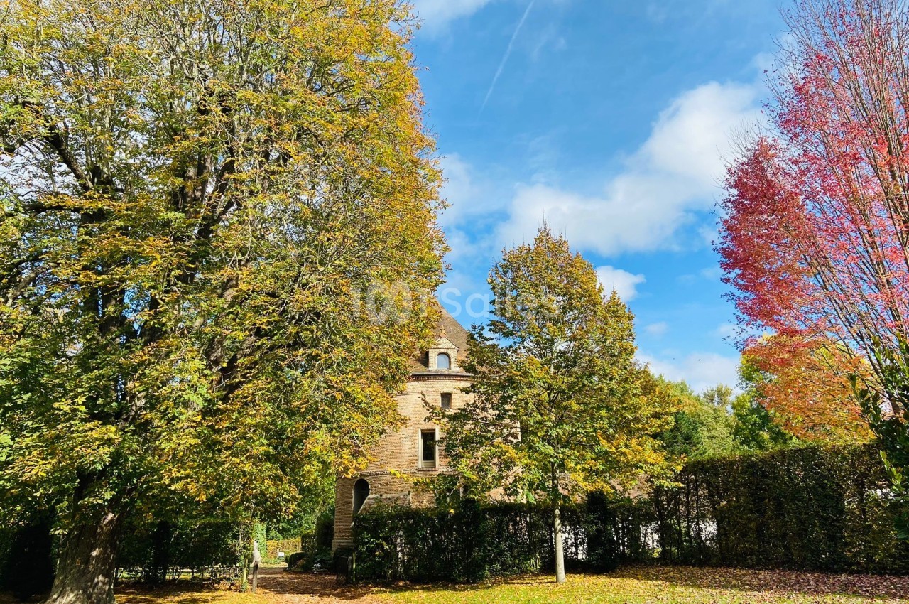 Maison en pierre entourée d'arbres aux feuillages d'automne sous un ciel bleu partiellement nuageux.