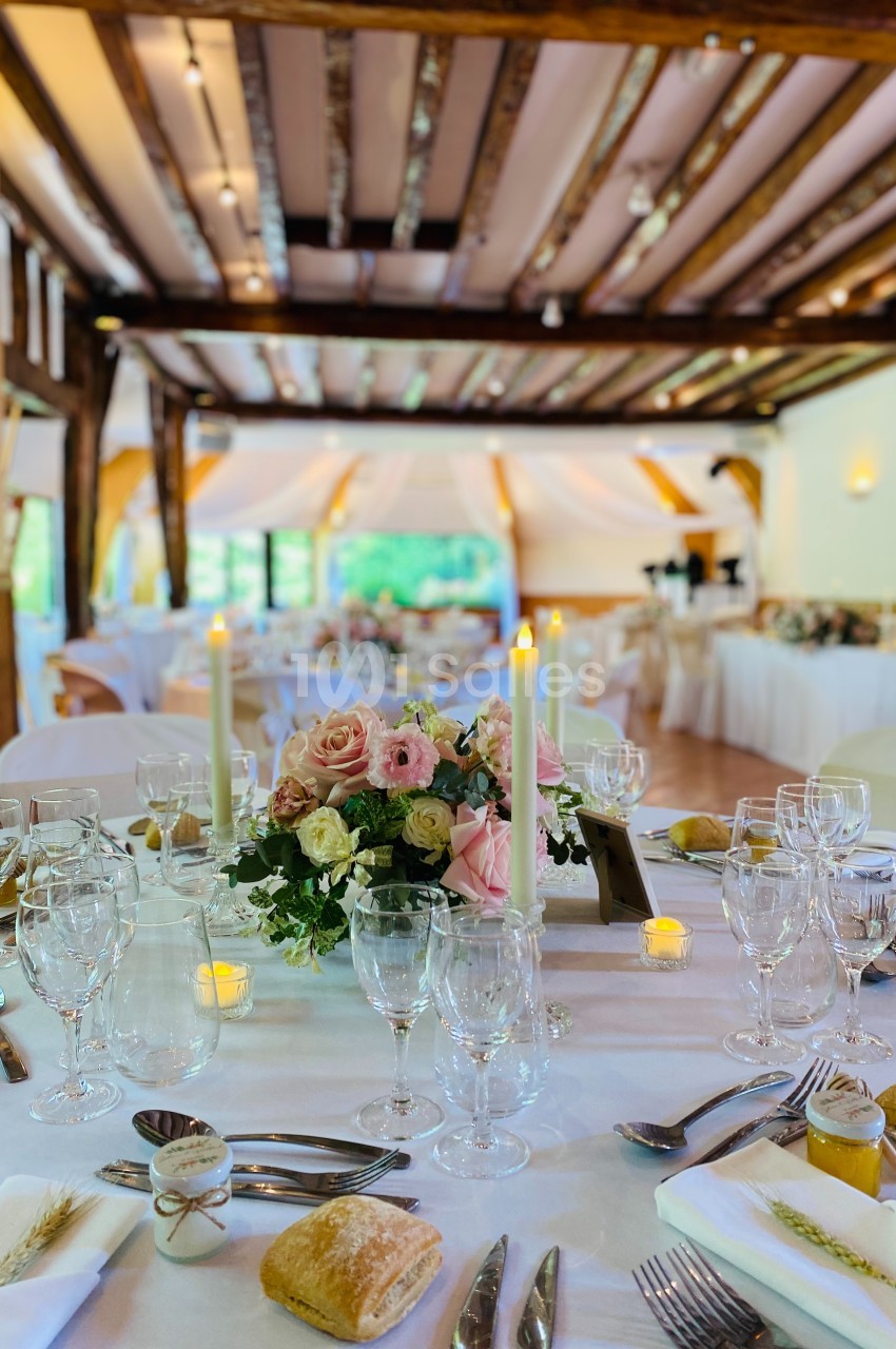 Table élégamment dressée avec des fleurs, bougies et vaisselle raffinée dans une salle de réception lumineuse.