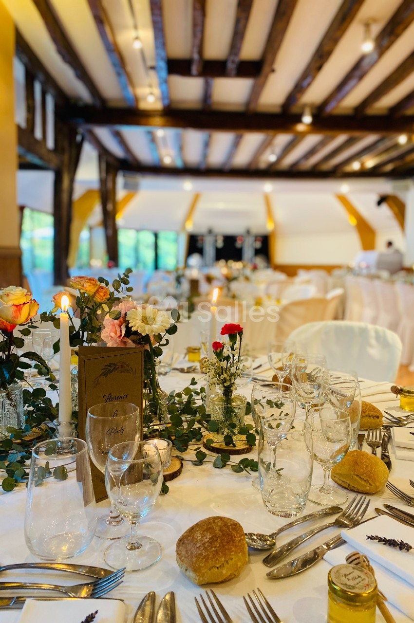 Salle de réception décorée avec des tables dressées, ornées de fleurs, bougies et vaisselle élégante.