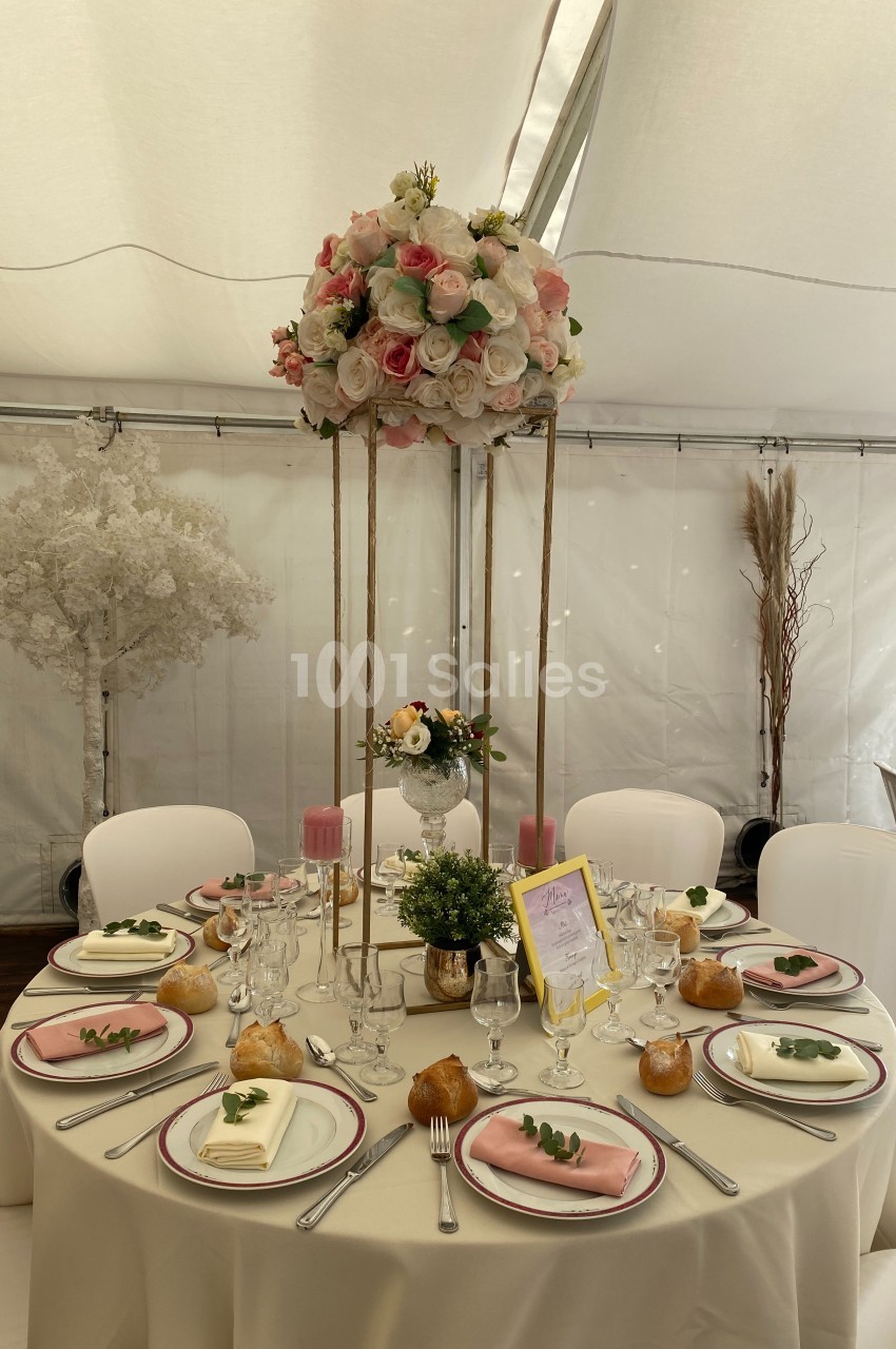 Table de réception élégante avec nappes blanches, vaisselle raffinée, centre de table fleuri et décorations pastel.