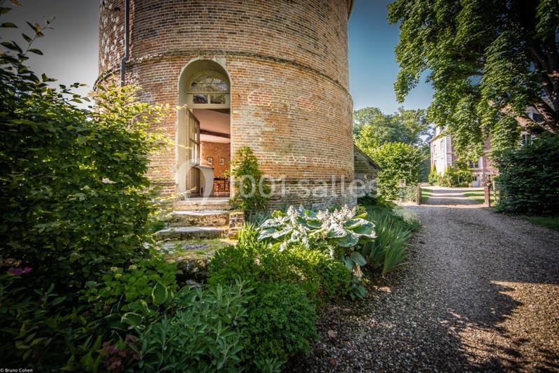 Entrée d'un bâtiment en briques rond avec porte ouverte, entouré de verdure et d'un chemin de gravier.