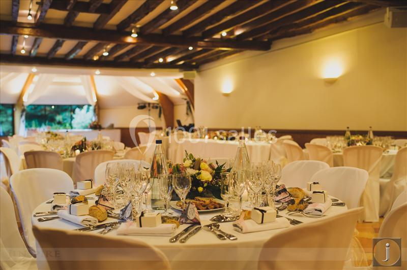 Salle de réception décorée avec des tables rondes dressées, nappes blanches, bouquets et couverts élégants.