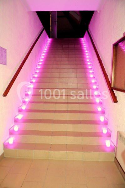 Escalier éclairé par des bougies roses alignées sur chaque marche dans un couloir intérieur.