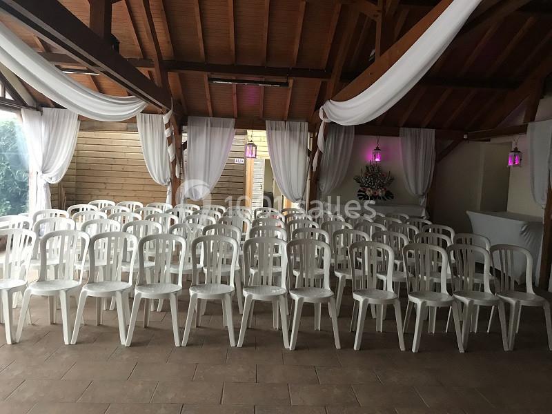 Salle décorée avec des rideaux blancs et des chaises en plastique alignées pour un événement ou une cérémonie.