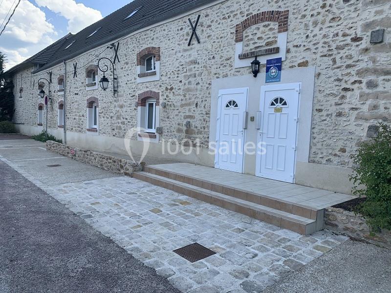 Façade en pierre d'un bâtiment avec deux portes blanches, lanternes murales et accès pavé devant l'entrée.