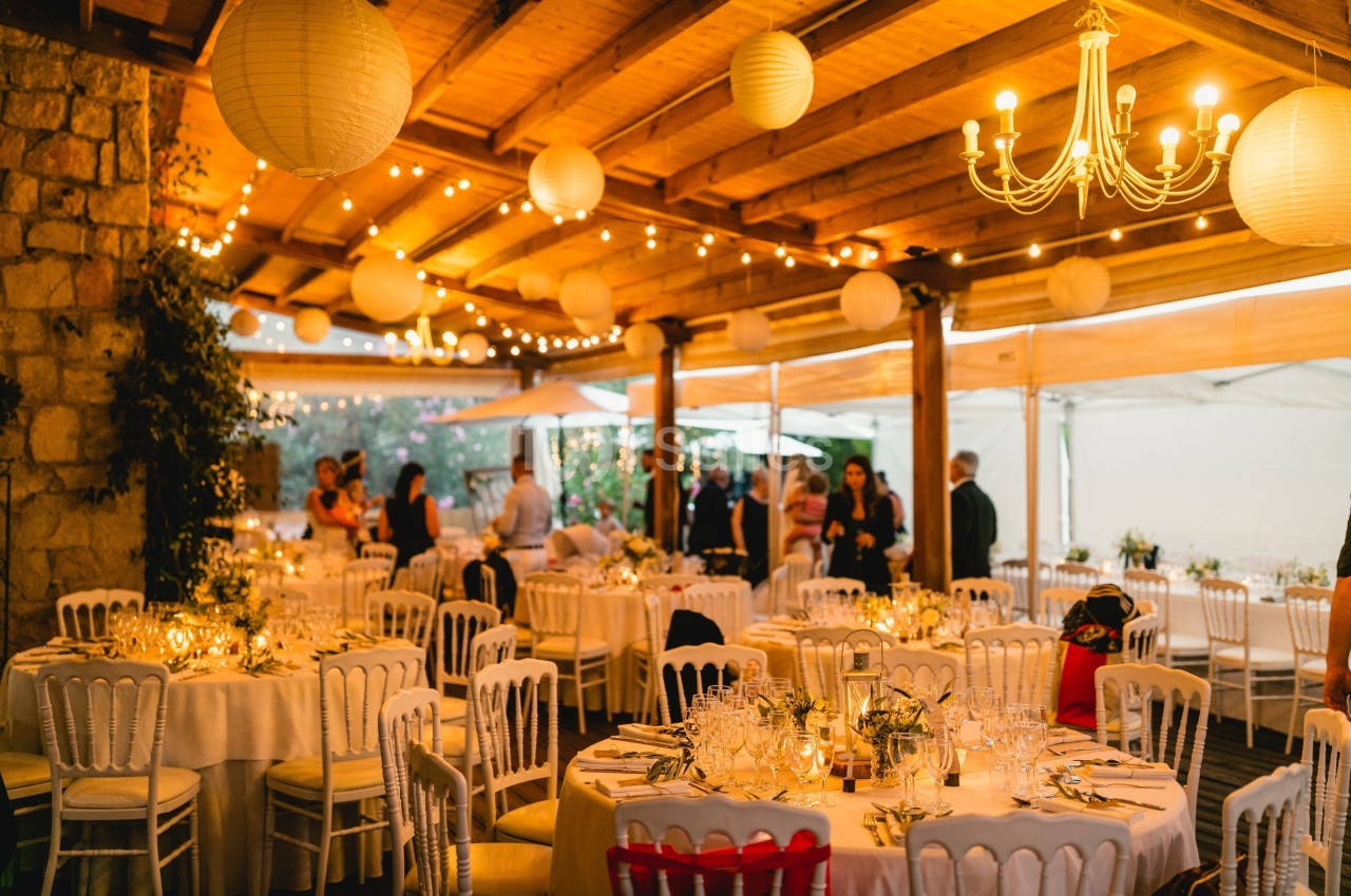 Salle de réception décorée avec des guirlandes lumineuses, des lanternes suspendues et des tables élégamment dressées.