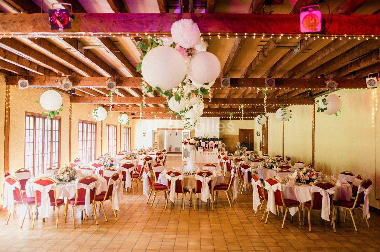 Salle de réception décorée avec des lanternes suspendues, des tables dressées et des chaises rouges.