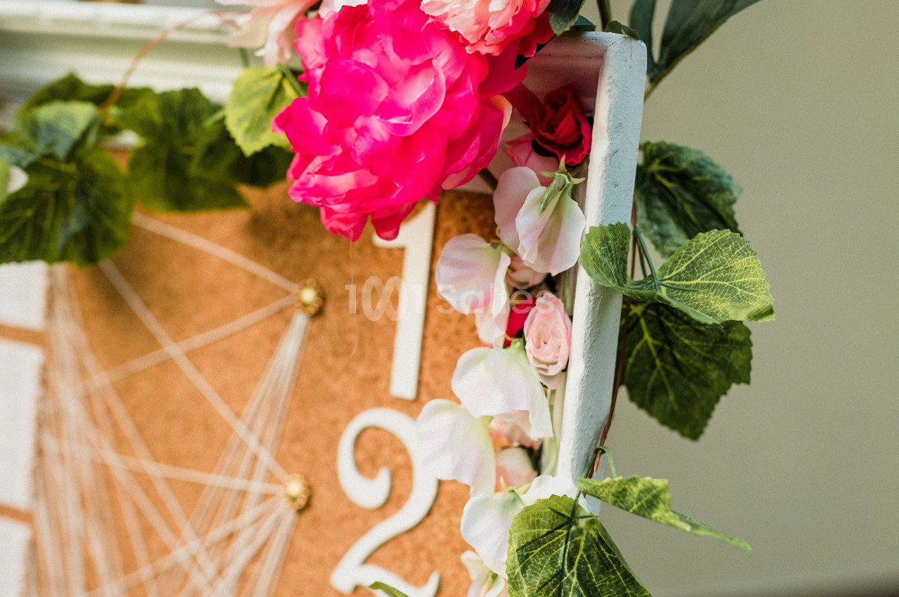 Fleurs roses et blanches avec feuillage décorant un tableau en liège orné de chiffres blancs.