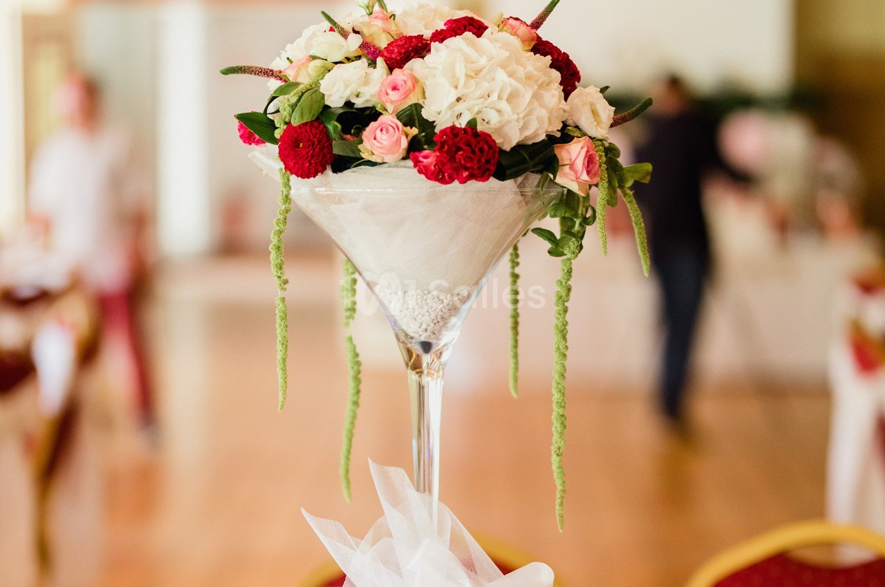 Centre de table floral dans un vase haut, composé de roses blanches et rouges avec des touches de verdure.