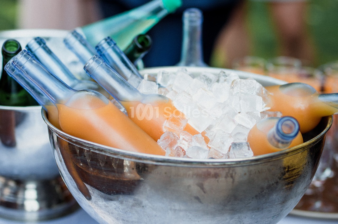 Bouteilles de jus orange disposées dans un saladier en métal rempli de glaçons.