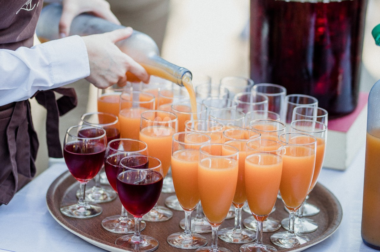 Un serveur verse du jus d'orange dans des verres alignés sur un plateau, à côté de verres de jus rouge.