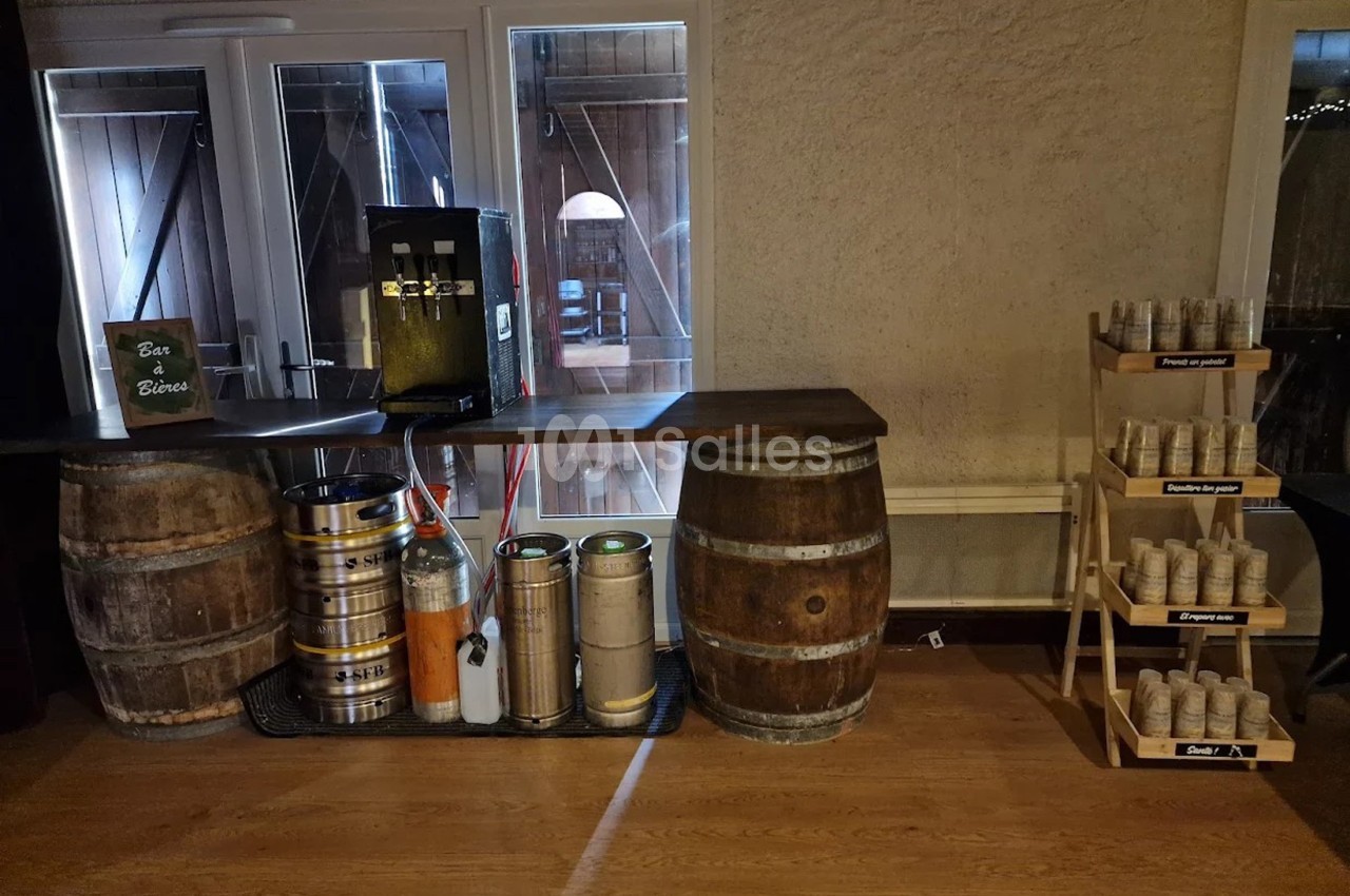 Bar en bois avec tonneaux, tireuse à bière, fûts métalliques et étagère contenant des gobelets en carton.