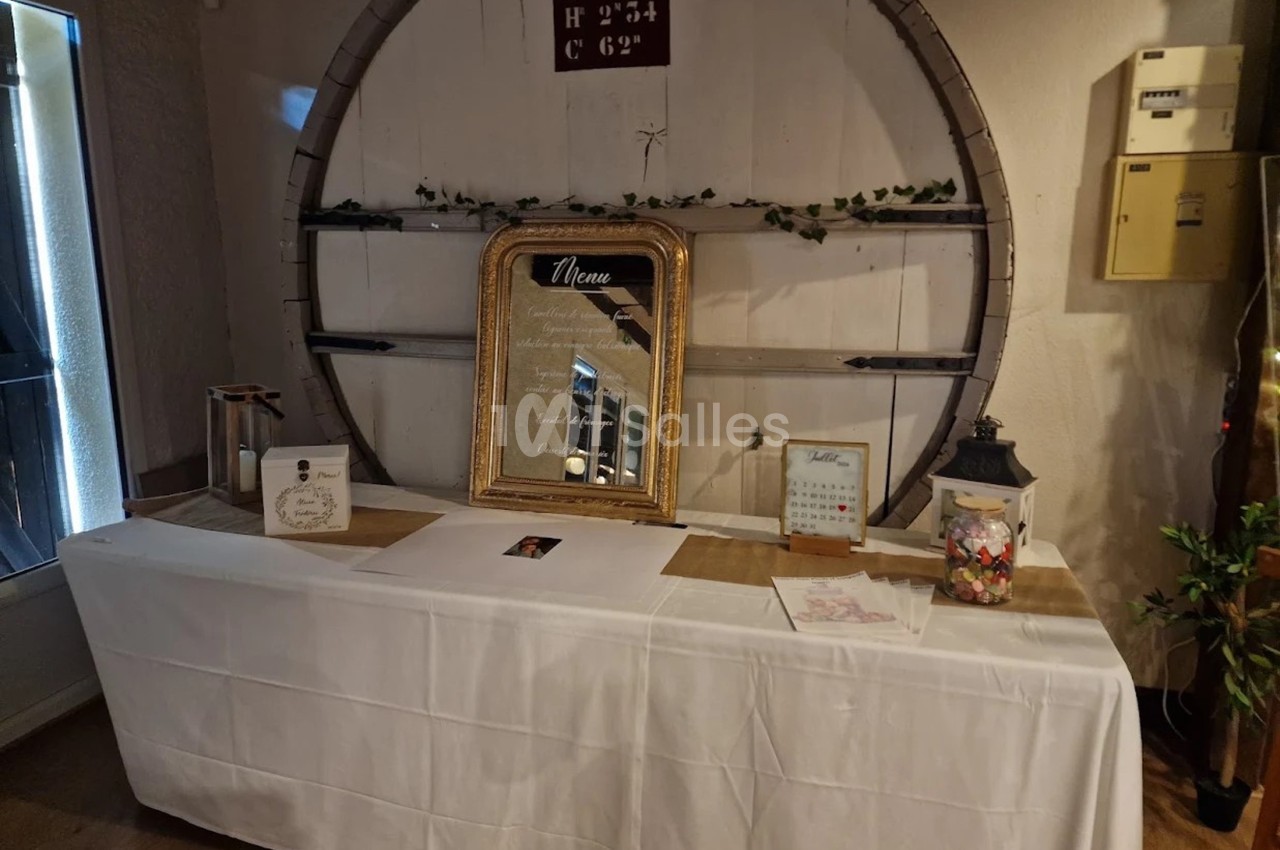 Table décorative avec nappe blanche, cadre doré affichant un menu, et divers éléments décoratifs dans un cadre rustique.