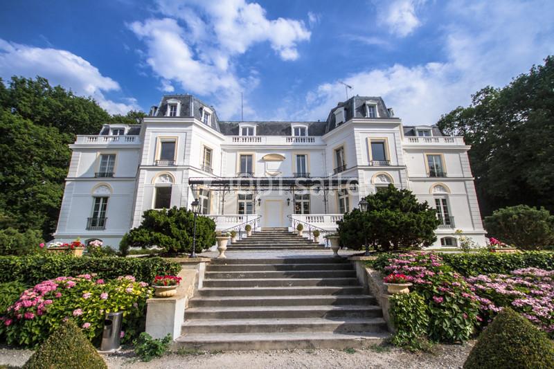 Façade d'un grand bâtiment blanc de style classique entouré de jardins fleuris et d'escaliers en pierre.