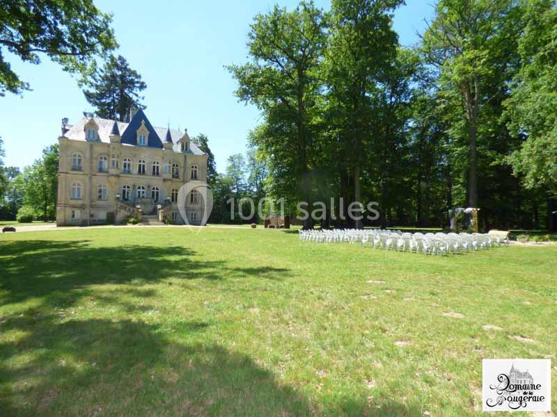Château entouré d'arbres avec des rangées de chaises blanches installées sur une pelouse pour un événement en plein air.
