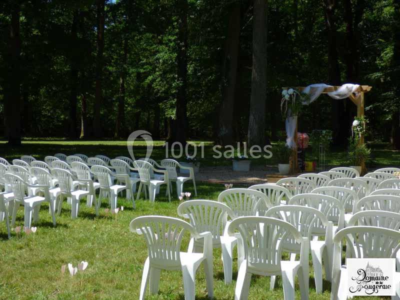 Chaises blanches disposées en rangées sur une pelouse, face à une arche décorée pour une cérémonie en plein air.