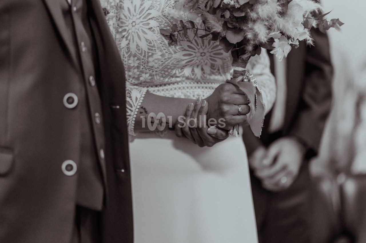 Un couple se tenant la main, vêtu de tenues de mariage, avec un bouquet de fleurs en arrière-plan.