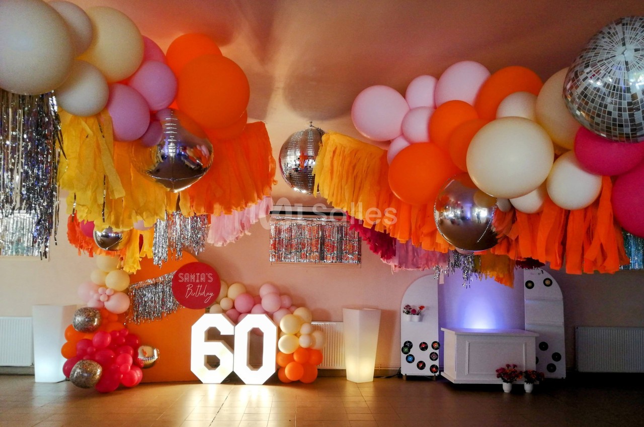 Décoration festive avec ballons colorés, guirlandes et chiffres lumineux ’60’ dans une salle de réception.