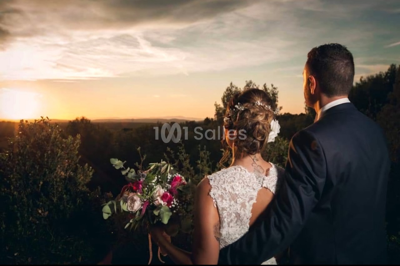 Un couple de dos, vêtu élégamment, regarde un coucher de soleil dans un paysage naturel.