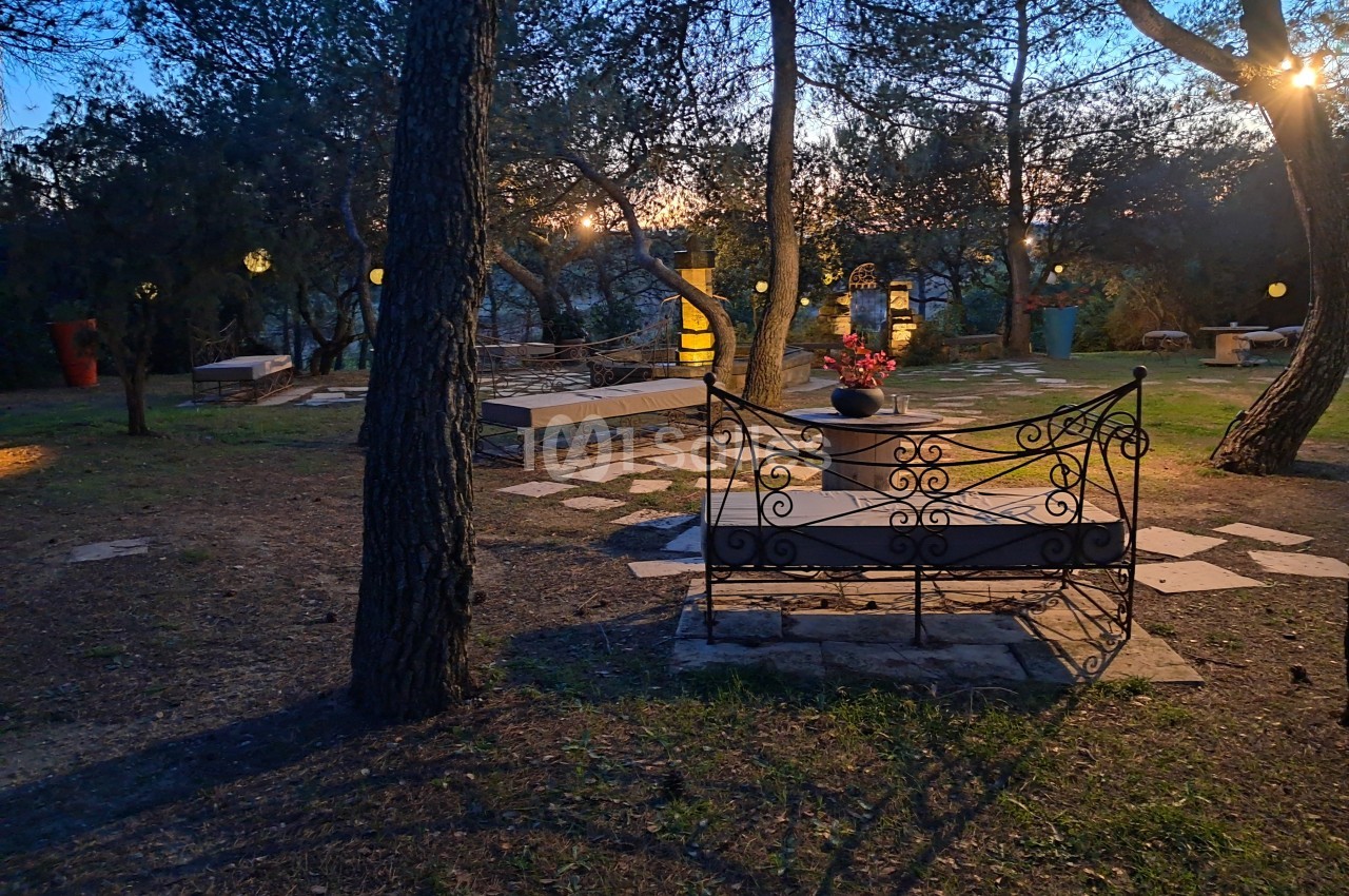 Banc en fer forgé dans un jardin boisé éclairé par des lampes suspendues au crépuscule.