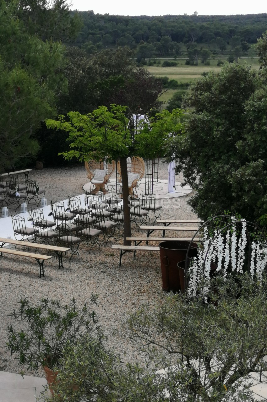 Espace extérieur aménagé avec des bancs, des chaises et des arbres, entouré de verdure et de décorations florales.