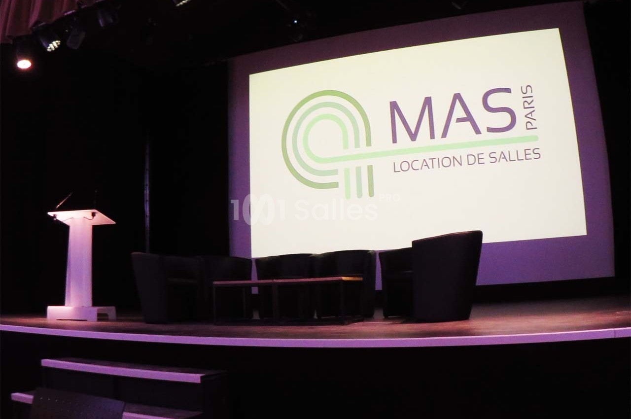 Salle de conférence avec un écran affichant le logo ’MAS Paris’ et un podium éclairé à gauche.