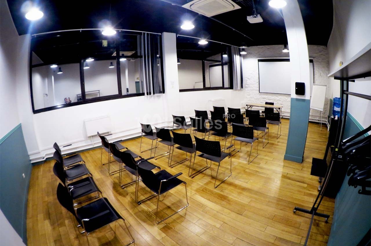 Salle de réunion lumineuse avec des chaises alignées, un écran de projection et un parquet en bois.