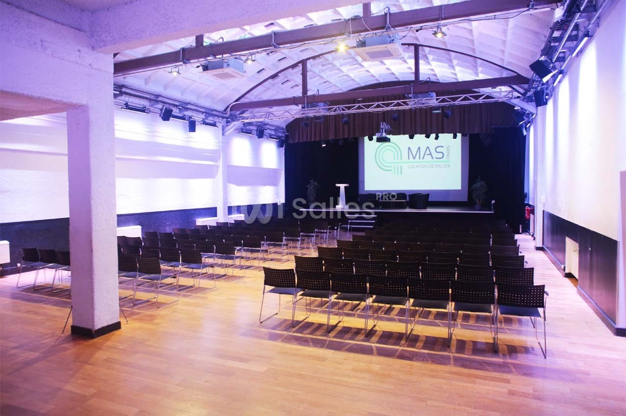 Salle de conférence lumineuse avec des rangées de chaises, une scène équipée et un écran de projection affichant un logo.
