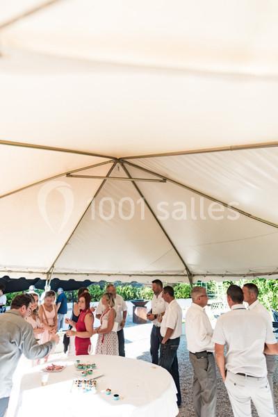Des personnes discutent sous une grande tente blanche lors d'un événement en extérieur, près d'une table avec des collations.