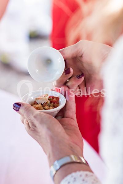 Une personne verse une sauce ou un liquide dans un petit bol contenant des aliments, en gros plan sur les mains.