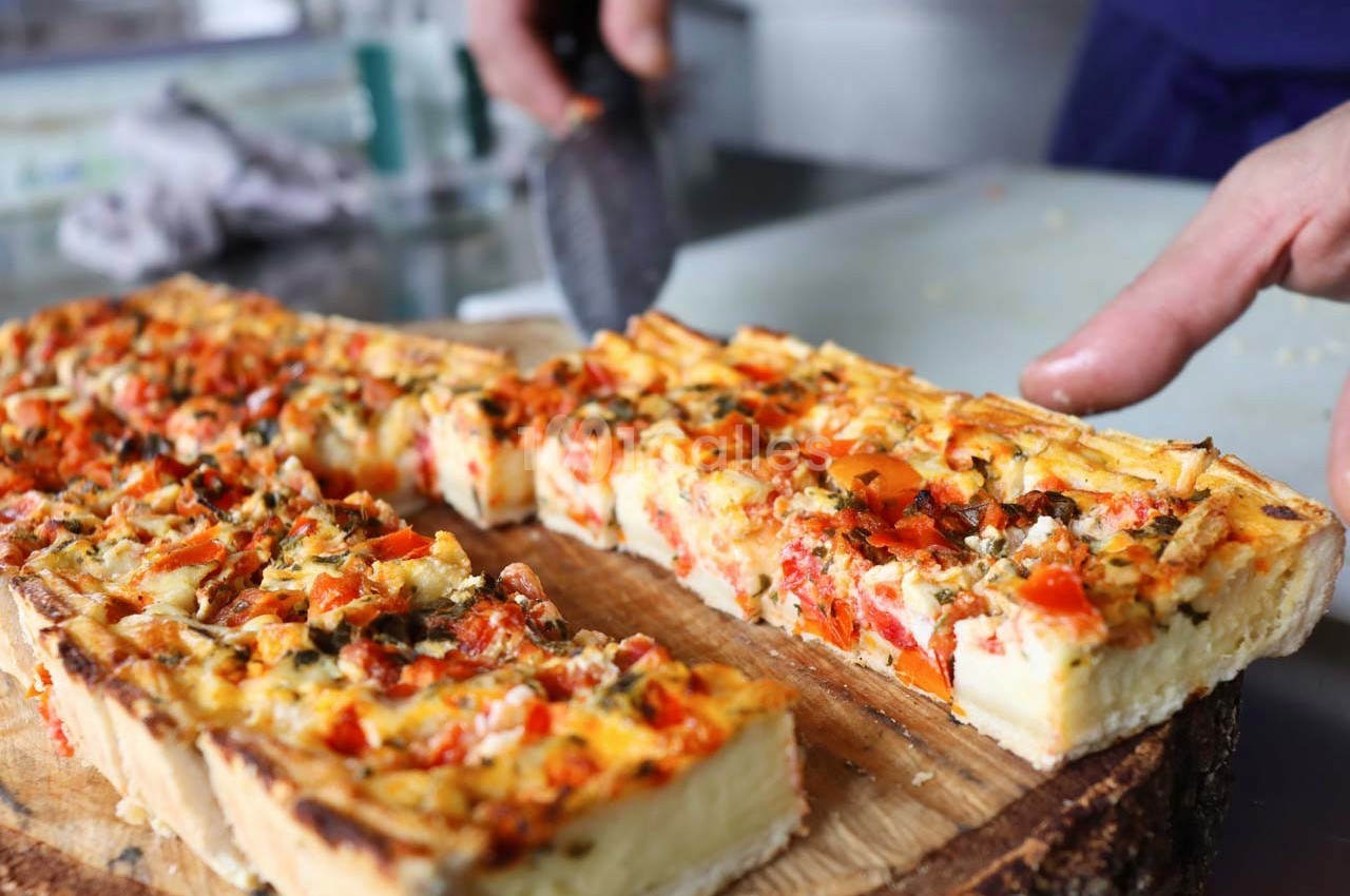 Quiche aux légumes colorés coupée en parts sur une planche en bois, avec une main tenant un couteau.