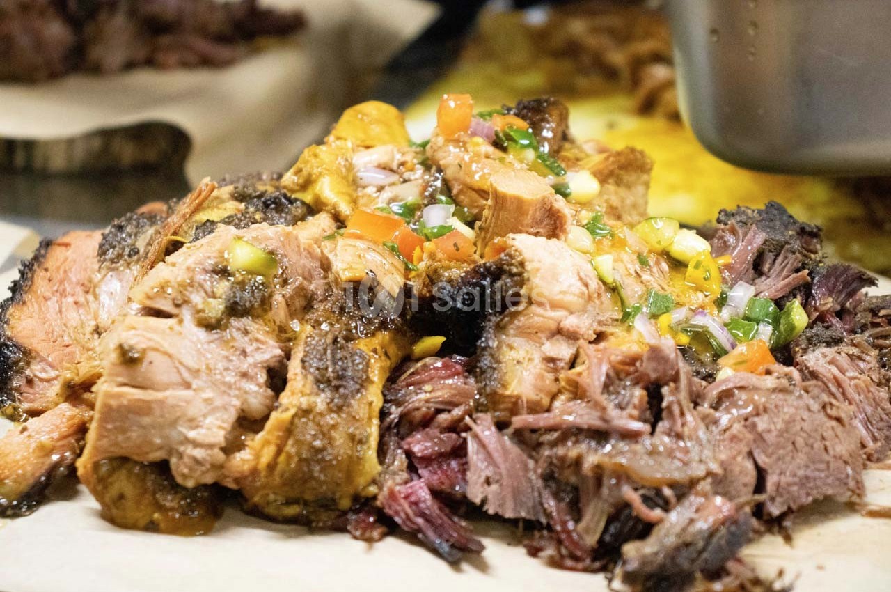 Viande effilochée garnie de légumes colorés et d'une sauce, servie sur une planche en bois.