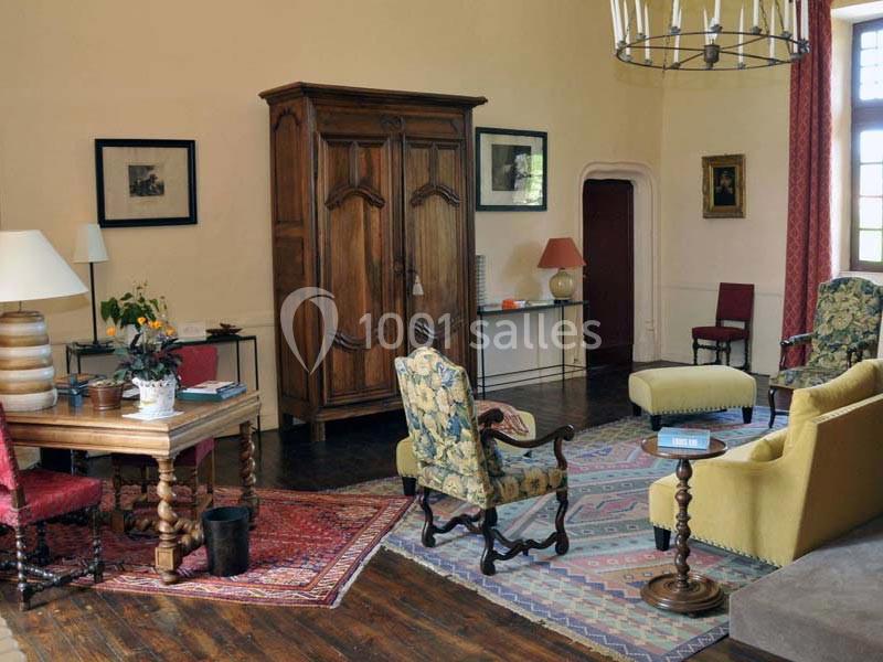 Salon avec mobilier ancien, tapis colorés, armoire en bois, fauteuils et lumière naturelle entrant par une fenêtre.