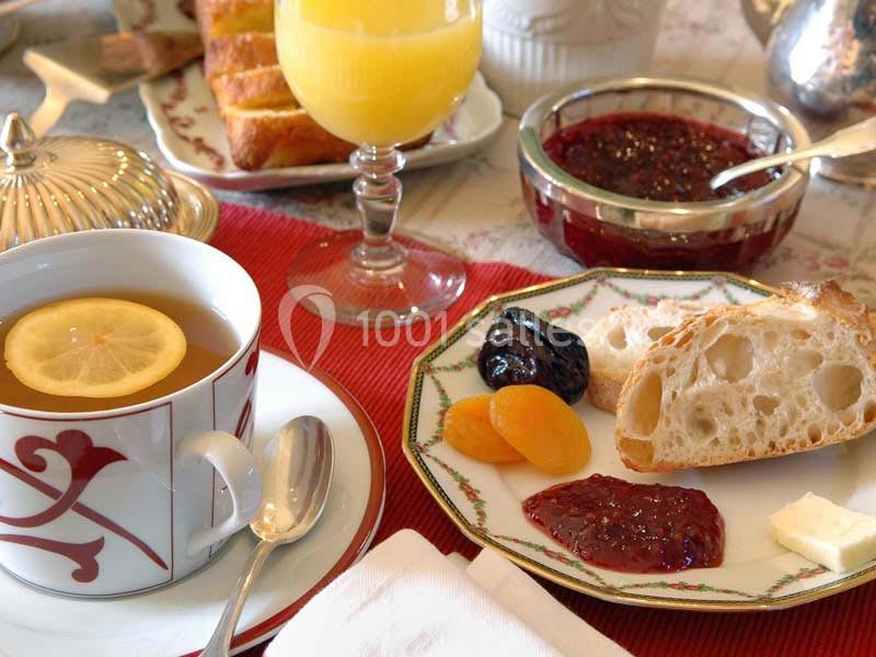 Petit-déjeuner avec thé au citron, jus d'orange, confitures, fruits secs et tranche de pain sur une table dressée.